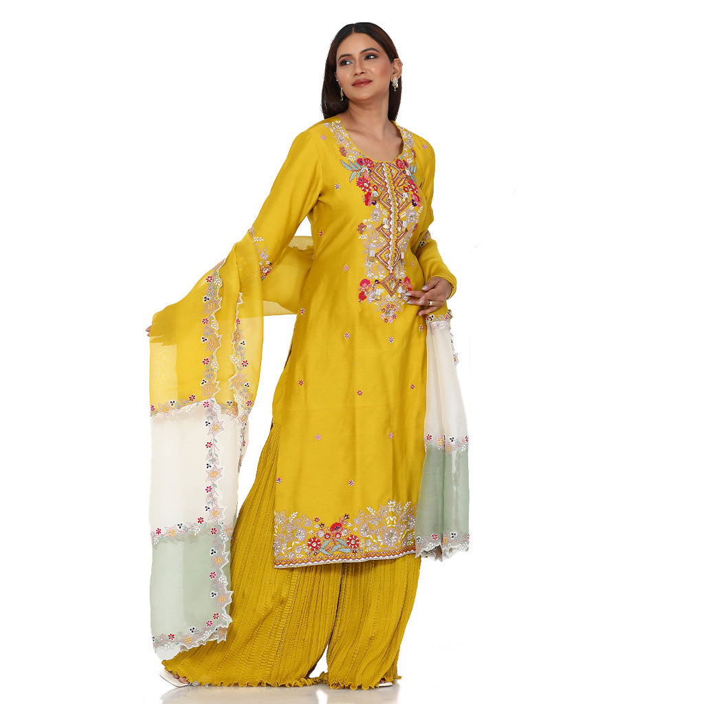 A woman standing and wearing Mustard Colored Kurta with Crush Sharara.