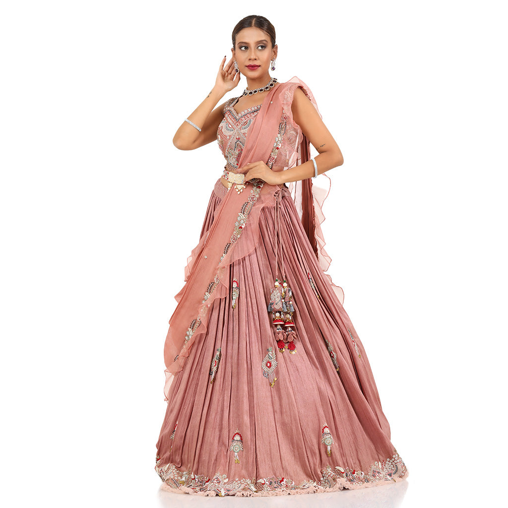 A woman standing and wearing Rose Pink lehenga set attaining a bridal attire.