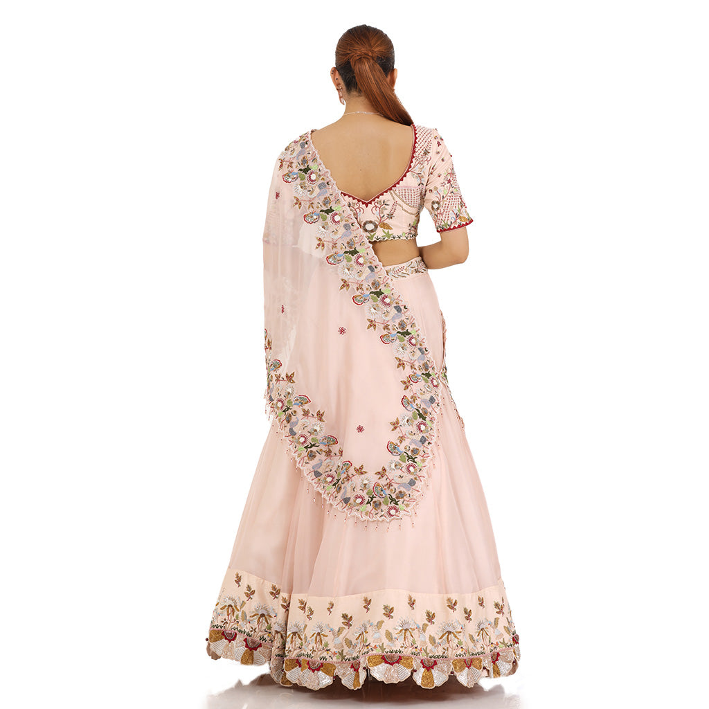 A woman standing and wearing pastel pink drape lehenga.