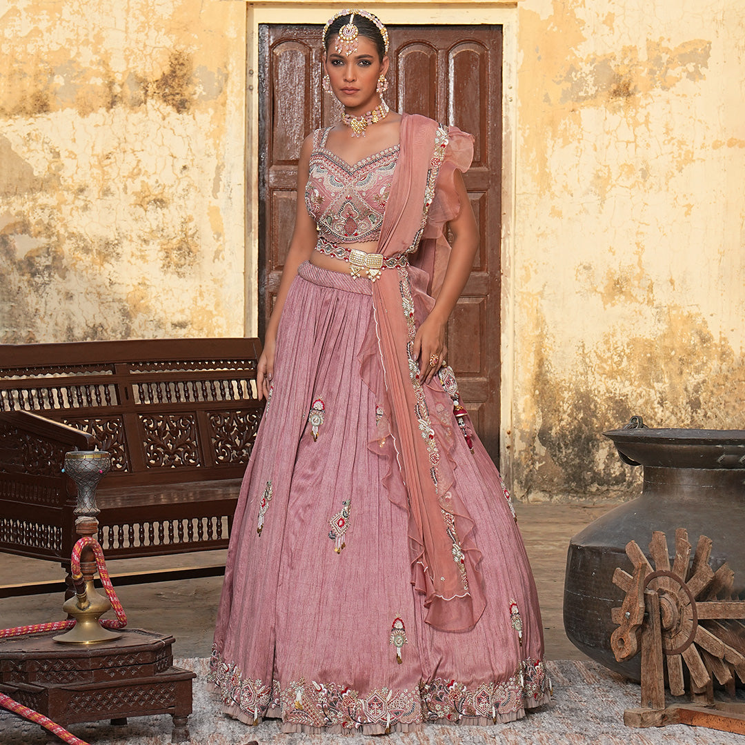 A woman standing and wearing Rose Pink lehenga set attaining a bridal attire.