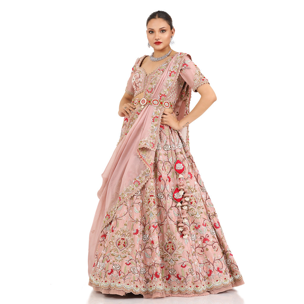 A woman standing and wearing Blush Pink Colored Rose Flower Lehenga Set.