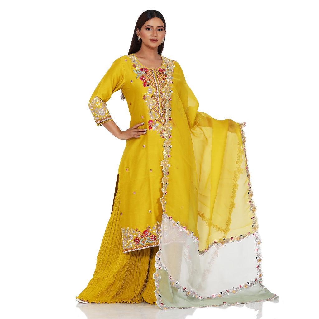 A woman standing and wearing Mustard Colored Kurta with Crush Sharara.