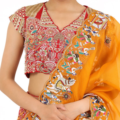 A woman standing and wearing Red orange Patola lehenga attaining a bridal attire.