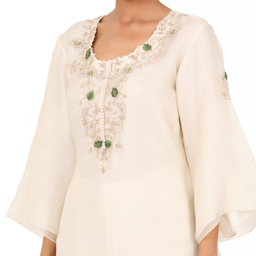 A woman standing and wearing Off White Kurta Sharara Set.