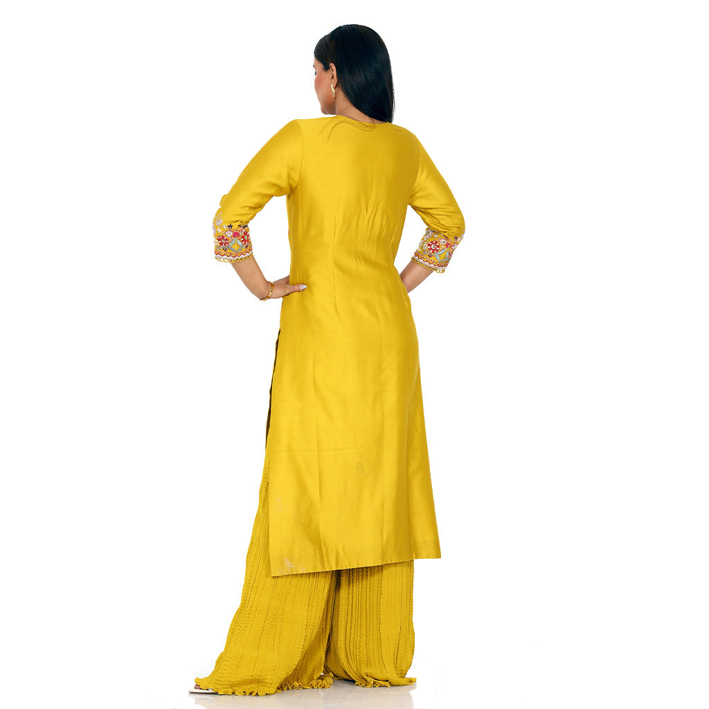 A woman standing and wearing Mustard Colored Kurta with Crush Sharara.