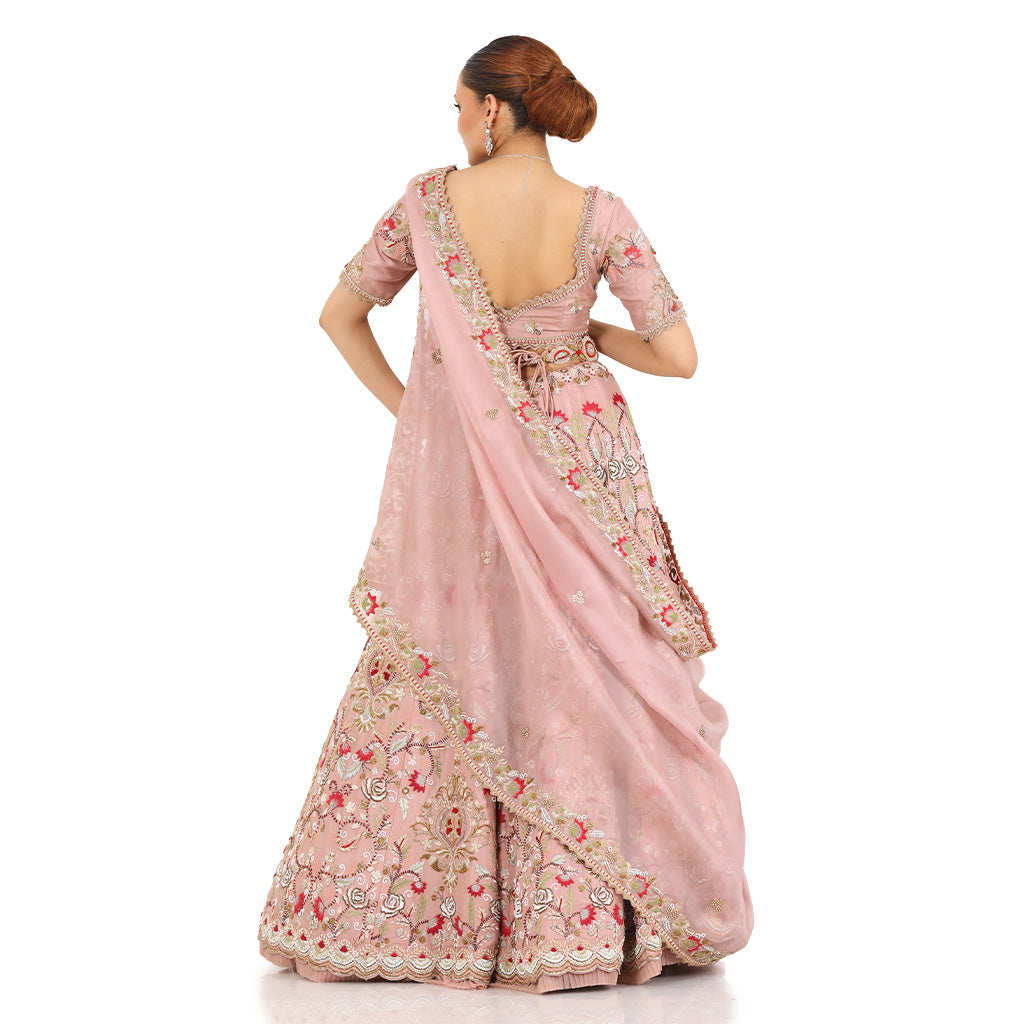 A woman standing and wearing Blush Pink Colored Rose Flower Lehenga Set.