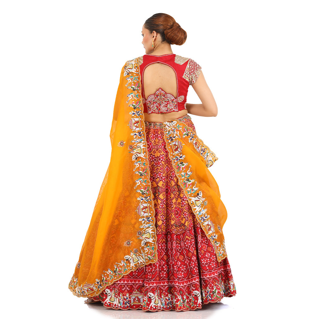 A woman standing and wearing Red orange Patola lehenga attaining a bridal attire.