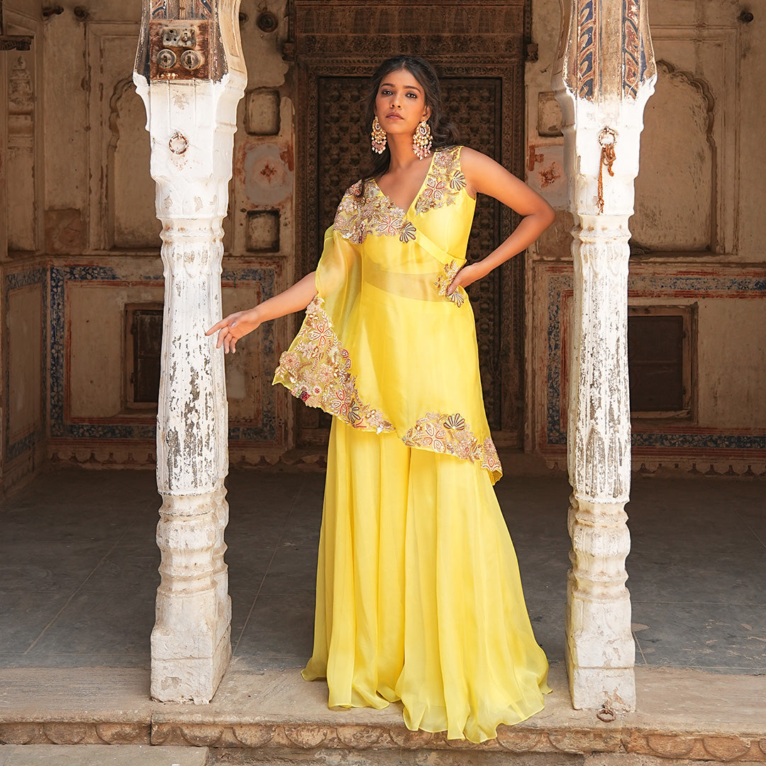 A woman standing and wearing Yellow Colored One Shoulder Poncho.