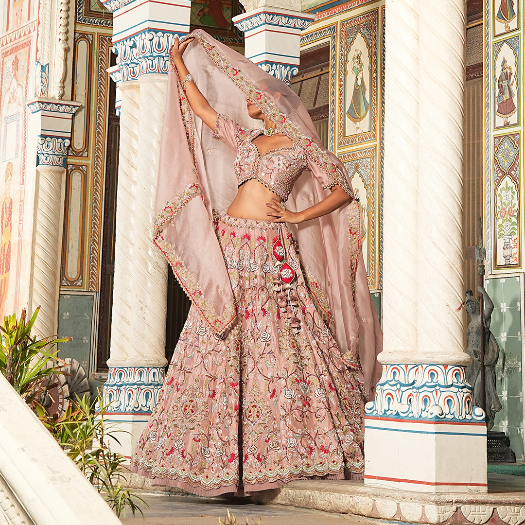 A woman standing and wearing Blush Pink Colored Rose Flower Lehenga Set.